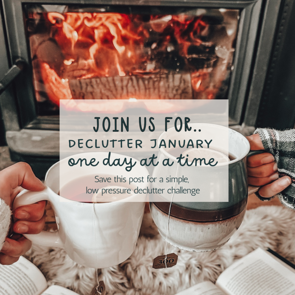 Two people holding mugs of tea in front of a lit fireplace with text overlay reading, “Join us for Declutter January, one day at a time.”