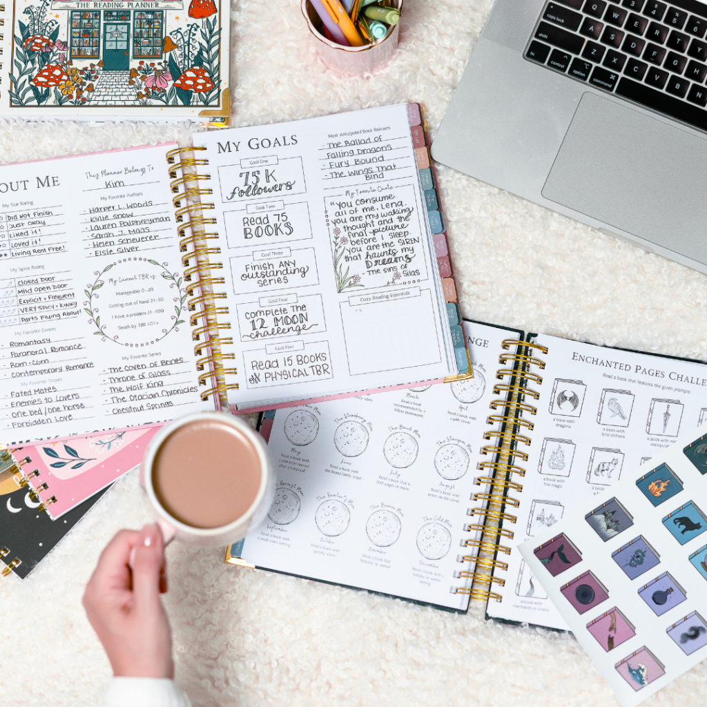 The Reading Planner open to a filled-in Goals page, with coffee, pens, and colorful tabs on a cozy desk